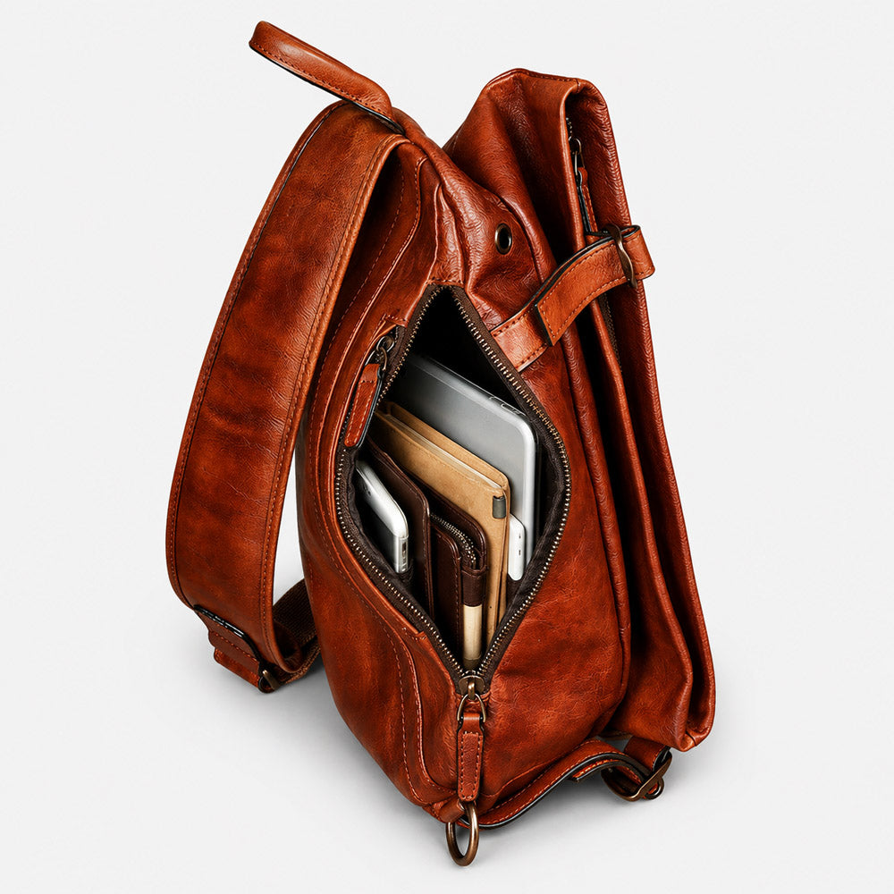 Open interior of brown leather shoulder bag showing space for an 11-inch tablet, mirrorless camera, wallet, and travel essentials