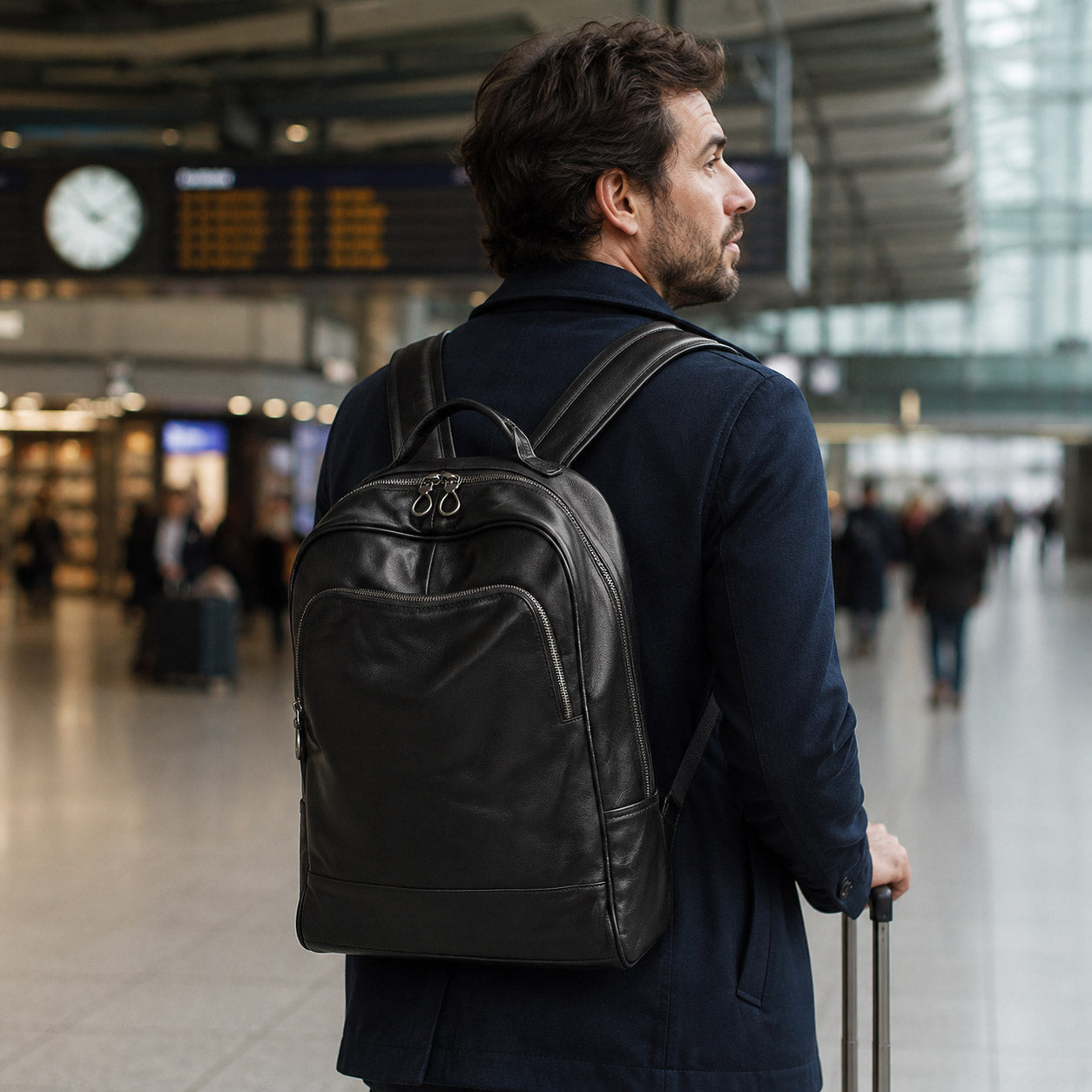 Traveller wearing the black leather backpack at a train station with a rolling suitcase